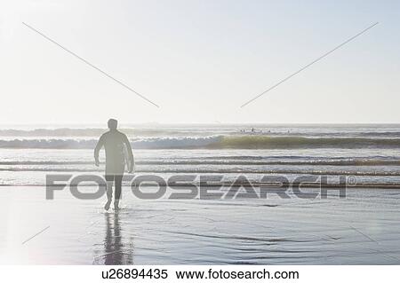 Stock Photography - Surfer carrying surfboard out of water. Fotosearch