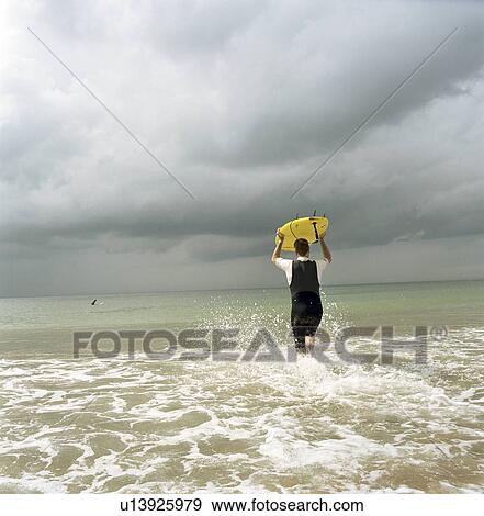 Stock Photo - Surfer running into water at beach. Fotosearch