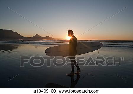 Stock Image - Surfer walking on beach. Fotosearch