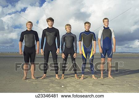 Stock Image - Surfers standing in row on beach. Fotosearch