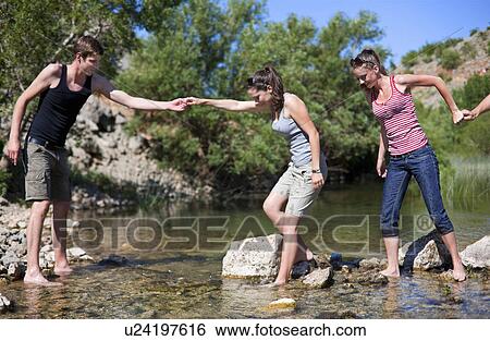 Stock Photograph - Teenagers crossing rocky river. Fotosearch