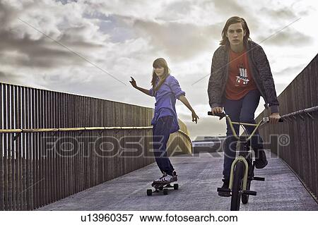 Teenagers riding bicycle and skateboard View Large Photo Image Stock Photo - Teenagers riding bicycle and skateboard. Fotosearch