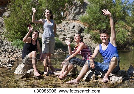 Stock Photograph - Teenagers waving from rocky river. Fotosearch