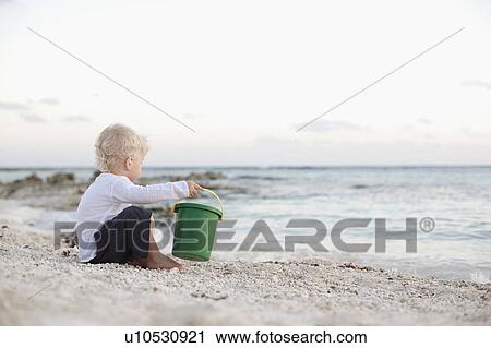 Stock Image - Toddler boy playing with sand on beach. Fotosearch