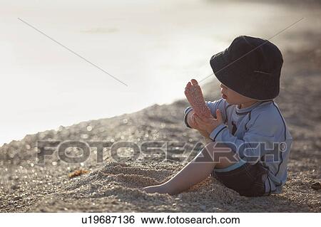 Stock Photograph - Toddler boy playing with sand on beach. Fotosearch