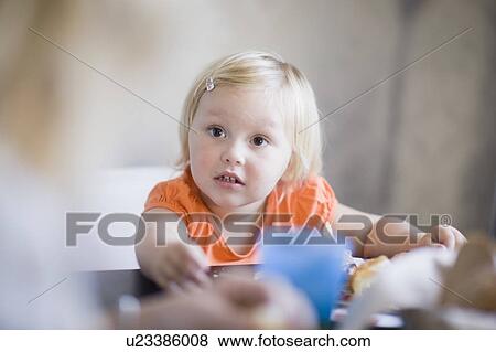 Stock Photo - Toddler girl eating at dinner table. Fotosearch