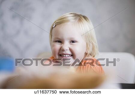 Stock Image - Toddler girl smiling at dinner table. Fotosearch