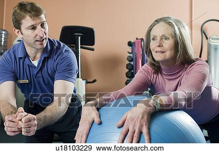 Stock Photo - Trainer helping older woman exercise. Fotosearch
