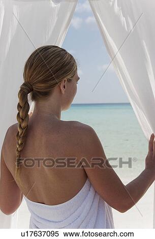 Stock Photography - Woman admiring beach through curtains. Fotosearch