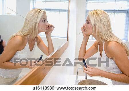 Stock Photograph - Woman applying makeup in mirror. Fotosearch