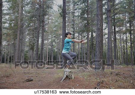 Stock Image - Woman balancing on stump in forest. Fotosearch