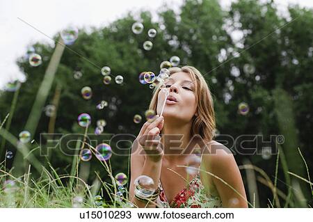 Stock Image - Woman blowing bubbles in field. Fotosearch