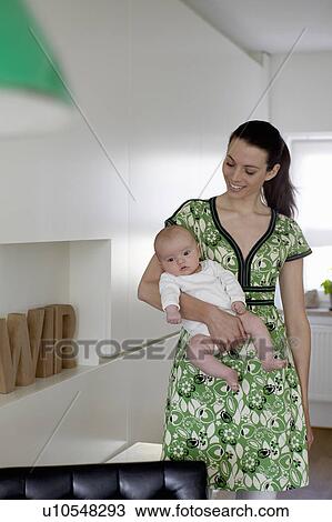 Stock Image - Woman carrying baby at home. Fotosearch