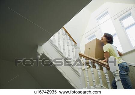 Stock Photography - Woman carrying cardboard box upstairs. Fotosearch