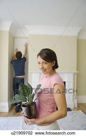 Stock Image - Woman carrying plant in new home. Fotosearch