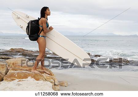 Stock Photo - Woman carrying surfboard on beach. Fotosearch