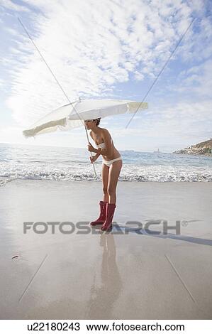 Stock Image - Woman carrying umbrella on beach. Fotosearch
