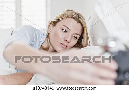 Woman checking alarm clock in bed View Large Photo Image Stock Photography - Woman checking alarm clock in bed. Fotosearch