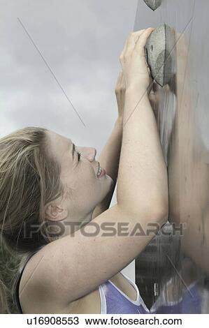 Stock Image - Woman climbing rock wall outdoors. Fotosearch