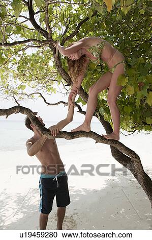 Stock Image - Woman climbing tree on tropical beach. Fotosearch