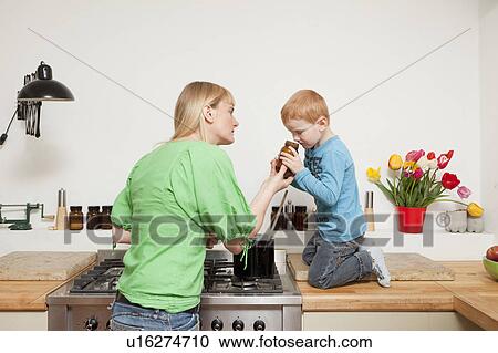 Stock Image - Woman cooking with son in kitchen. Fotosearch