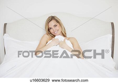 Stock Photo - Woman covering herself with duvet in bed. Fotosearch
