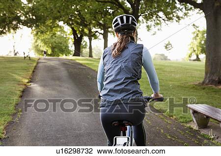 Stock Image - Woman cycling uphill at park. Fotosearch
