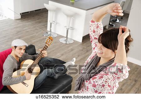 Stock Image - Woman dancing as boyfriend plays music. Fotosearch