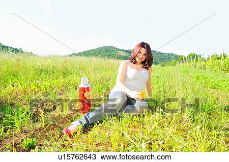 Stock Image - Woman drinking from thermos in field. Fotosearch