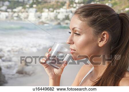 Stock Image - Woman drinking glass of water on beach. Fotosearch