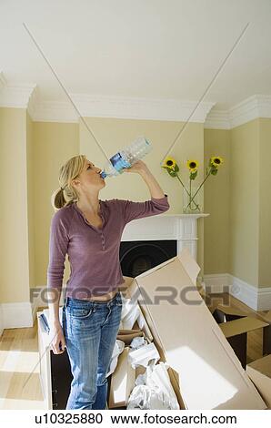 Stock Image - Woman drinking water in new home. Fotosearch