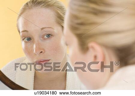 Stock Image - Woman examining her face in mirror. Fotosearch