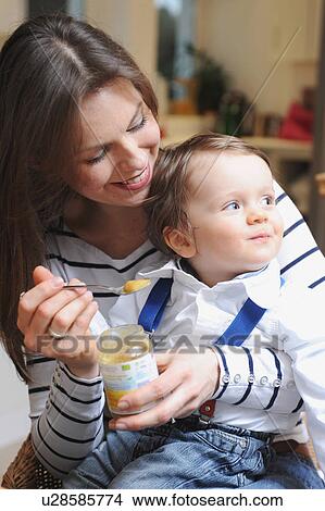 Picture - Woman feeding toddler son baby food. Fotosearch