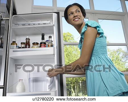 Stock Image - Woman getting water pitcher from fridge. Fotosearch