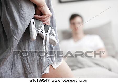 Woman hiding baby shoes from boyfriend View Large Photo Image Stock Photo - Woman hiding baby shoes from boyfriend. Fotosearch
