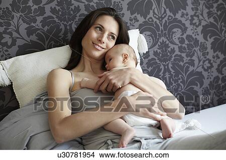 Woman holding baby in bed View Large Photo Image Picture - Woman holding baby in bed. Fotosearch