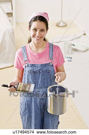 Picture - Woman holding paint bucket at home. Fotosearch