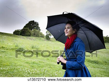 Stock Image - Woman holding umbrella in field. Fotosearch