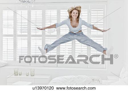Stock Image - Woman jumping on bed. Fotosearch
