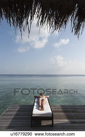Stock Image - Woman laying on deck overlooking sea. Fotosearch