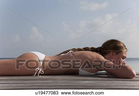 Stock Image - Woman laying on deck overlooking sea. Fotosearch