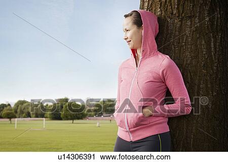 Woman leaning against tree in park View Large Photo Image Stock Image - Woman leaning against tree in park. Fotosearch