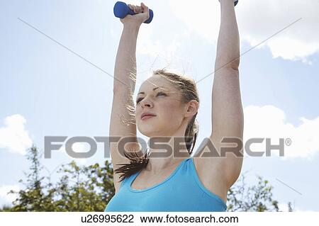 Stock Image - Woman lifting weights outdoors. Fotosearch