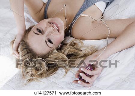 Stock Image - Woman listening to headphones on bed. Fotosearch