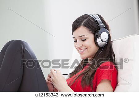 Stock Image - Woman listening to headphones on couch. Fotosearch