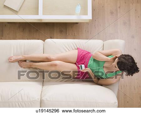 Stock Photograph - Woman listening to headphones on couch. Fotosearch