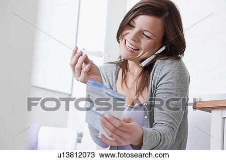 Stock Image - Woman on cell phone with pregnancy test. Fotosearch