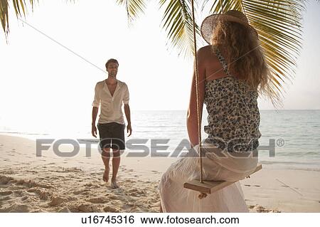 Stock Photograph - Woman on swing with boyfriend at beach. Fotosearch