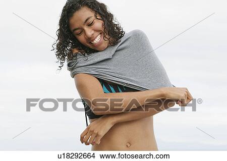 Picture - Woman pulling on shirt outdoors. Fotosearch