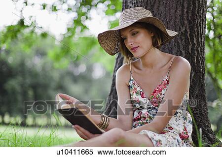 Woman reading against tree in field View Large Photo Image Stock Photography - Woman reading against tree in field. Fotosearch